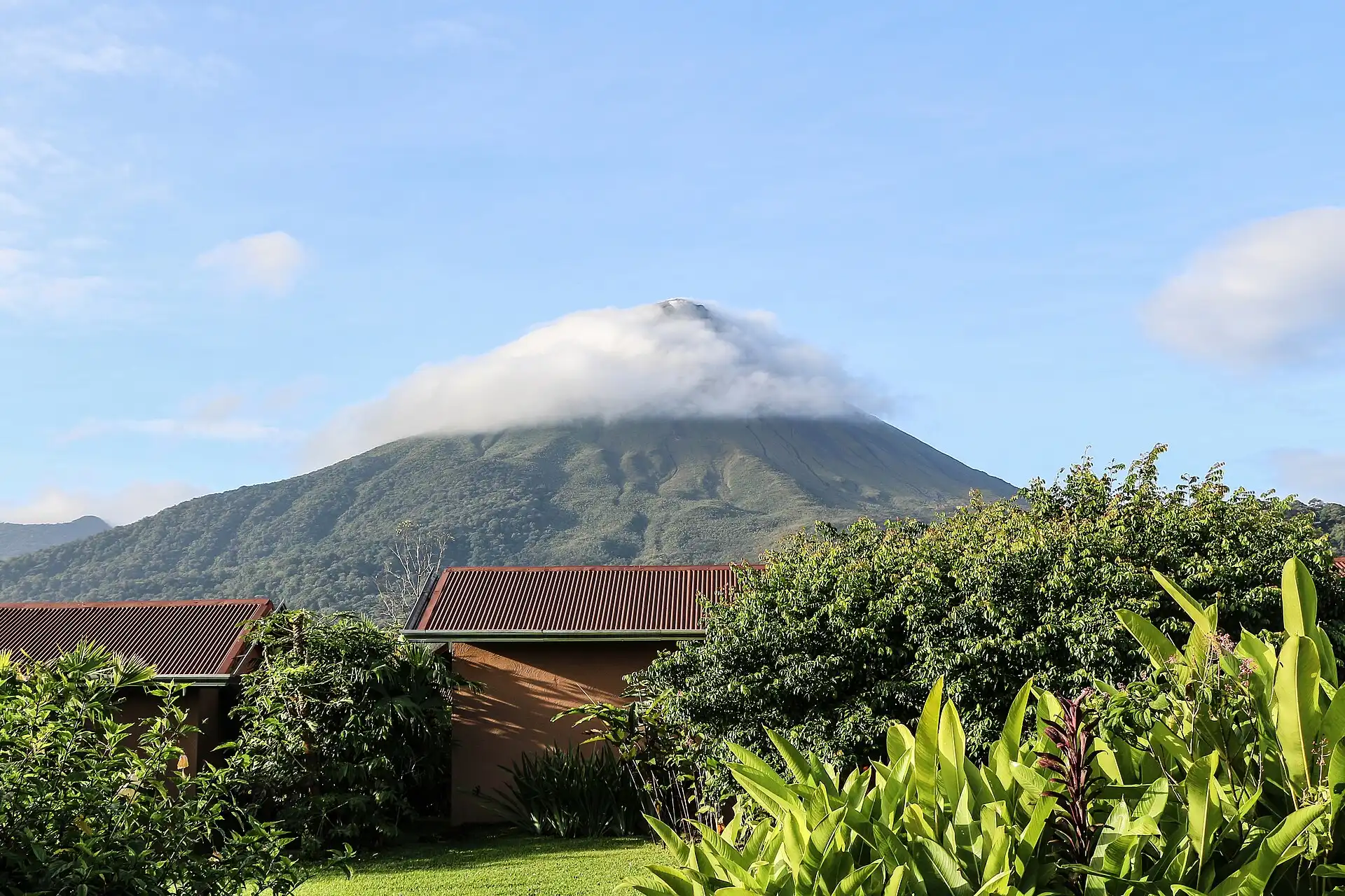 Arenal volcano with its peak in cloud, seen over a garden in Costa Rica.