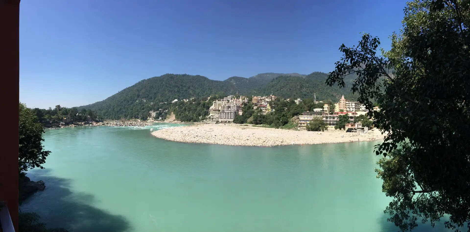 The Ganges at Rishikesh, with the town and forested hills beyond a gravel bar.